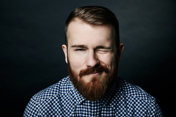 Winking red bearded man studio portrait on dark background