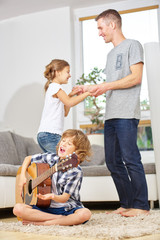Junge spielt Gitarre und Vater und Mädchen tanzen