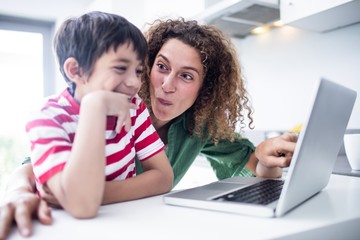 Mother and son using laptop in kitchen