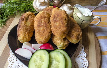 Patties with potatoes, mushrooms and a dill on with radishes and cucumbers on a black platter
