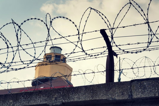 Filtered vintage guarding tower behind barbed wire fence prison walls