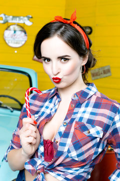 Portrait of Young Woman With Pinup Hair Style And Makeup holding candy in hand and  Posing In Retro Studio