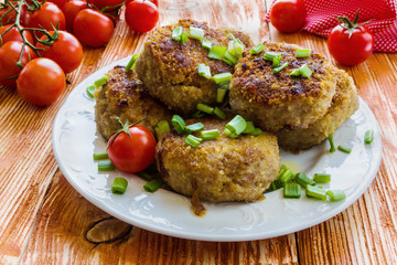 Roasted chicken cutlets with green onion on white plate and small cherry tomatoes on wooden background. 