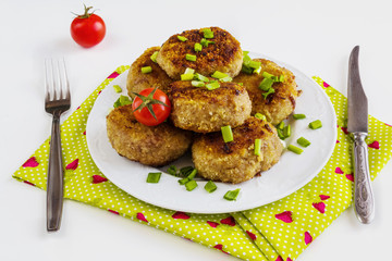 Roasted chicken cutlets with green onion on white plate and small cherry tomatoes on white table.