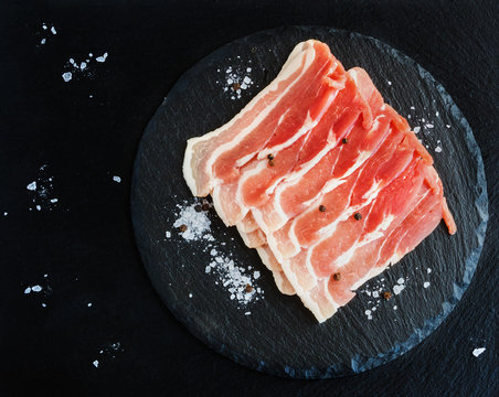 Raw Sliced Bacon On Black Stone Background. Top View.