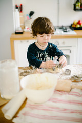 Little boy in the kitchen helping to cook the dough for baking
