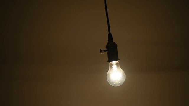 Swinging tungsten light bulb in the dark