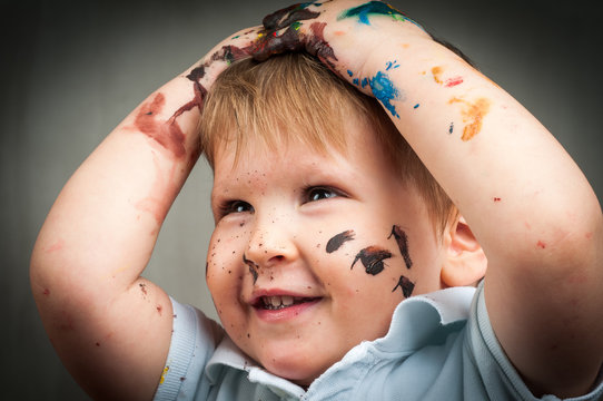 Portrait of a cute little boy messily playing with paints