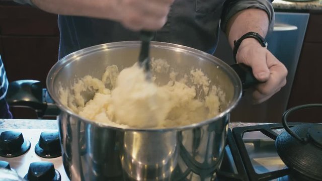 Man Mashing Boiled Potatoes With Butter In Cooking Pot