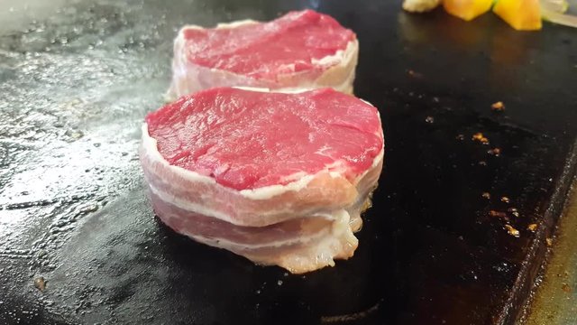 Frying bacon wrapped, filet mignon tournedos steaks, at a restaurant kitchens frying pan