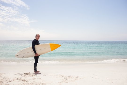 Portrait of senior man in wetsuit holding a surfboard