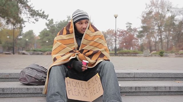 Kind young woman giving money to poor homeless man begging for help in street