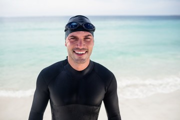Young man in wetsuit and swimming goggles standing on beach