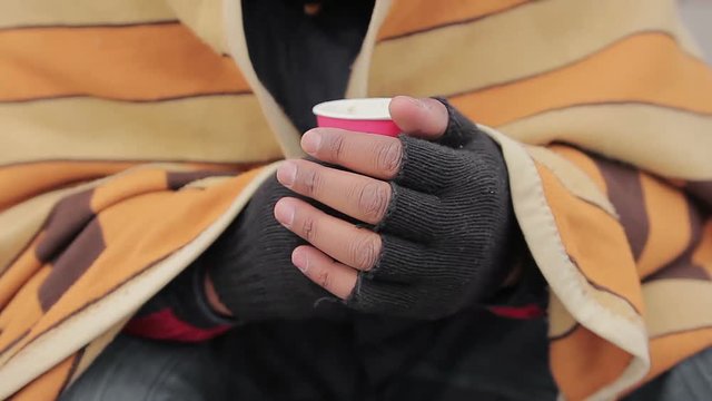 Needy person's hands holding warm drink in paper cup, closeup. Poverty issue