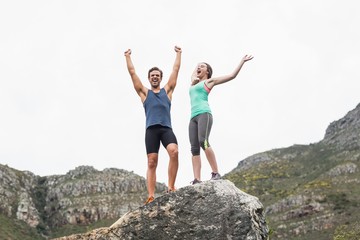 Excited young couple on rock against sky