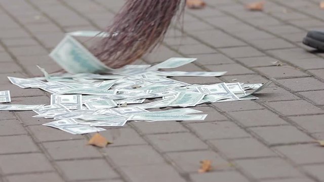 Person sweeping American dollars into pile in city street, depreciated assets