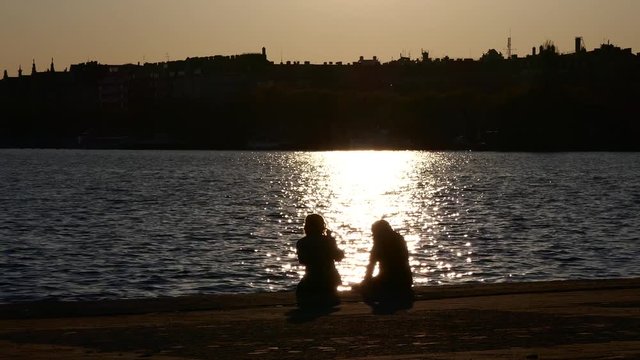 STOCKHOLM, SWEDEN, MAY 2016: A romantic silhouette couple sitting together near the sea with ray of sun light on the water during sunset