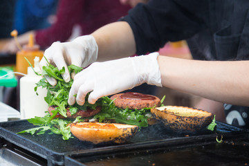 Chef making beef burgers outdoor on open kitchen international food festival event. Street food ready to serve on a food stall.