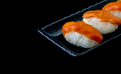 Salmon sushi nigiri in chopsticks over black background