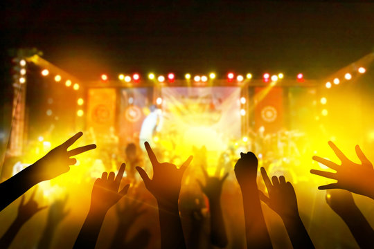 Audience with hands raised at a music festival and lights streaming down from above the stage. live concert, music festival, happy youth, luxury party, landscape exterior.