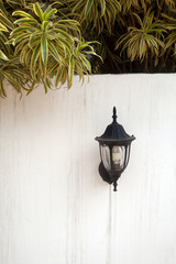 A black vintage lantern on a white fence wall with tree branches