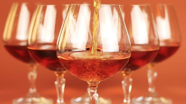 Close up of brandy being poured into snifter on brown background