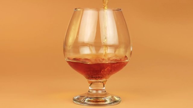 Close up of brandy being poured into snifter on brown background