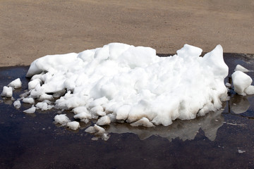 A large pile of dirty white snow lies on the asphalt road