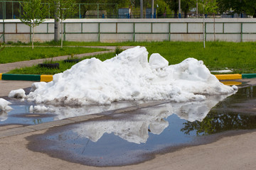 A large pile of dirty snow lying in the puddle on the asphalt ro