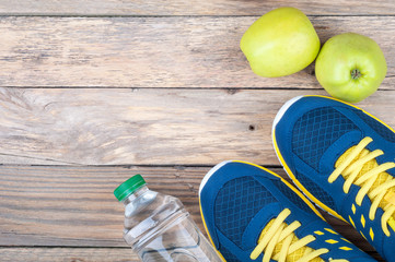 Running sport shoes, bottle of water and apple on wooden background top view. Active sports  life and healthy diet concept