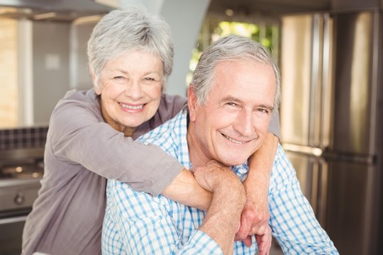 Portrait of cheerful senior couple embracing in kitchen