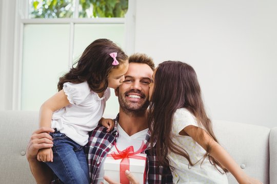 Father holding gift box and daughters kissing him 