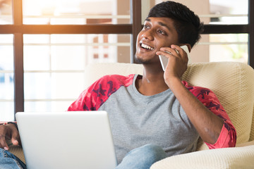 Fototapeta na wymiar teenage indian male using laptop and having phone conversation