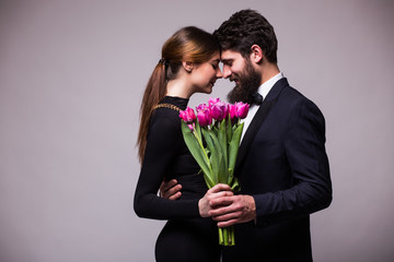 Young sweet couple with bucket of tulips on grey background