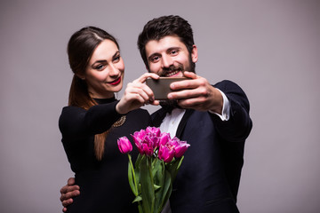 Young sweet couple with bucket of tulips take selfie from phone on grey background