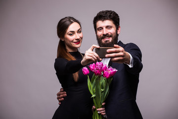 Young sweet couple with bucket of tulips take selfie from phone on grey background