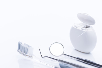 Dental floss and brush with basic dental tools on a white table