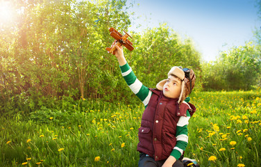 Boy playing in aviator hat with old plane at countryside