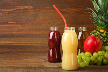 glass bottles of juice and an Apple with grapes and pineapple on the brown wooden background
