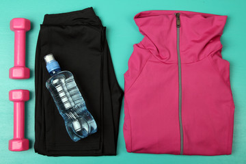sporting a pink shirt and black sweat pants with pink dumbbells near your water bottle on a turquoise background