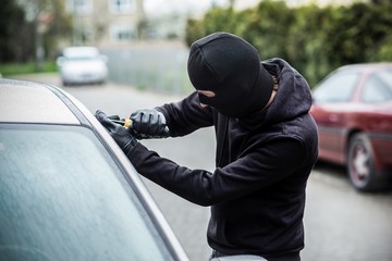 Car thief trying to break into a car with a screwdriver.