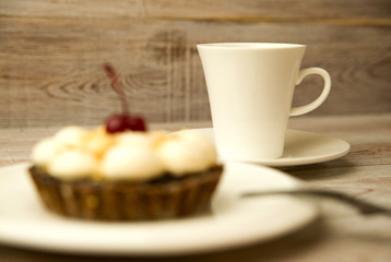 Cake with cherry and a cup on the table