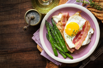 Breakfast with asparagus, egg, bacon and toast on dark rustic wooden background