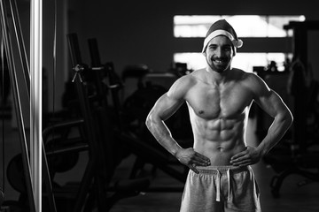 Fototapeta na wymiar Muscular Man Wearing Santa Claus Hat In Gym