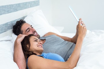 Happy young couple using tablet while lying on bed