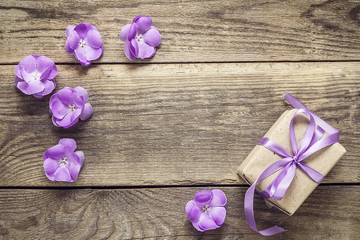 Gift box with ribbon, purple flowers on wood background with emp