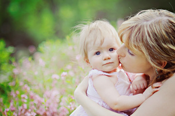 A portrait of mothers and daughters on the blooming meadow, mother kissing daughter on the cheek.