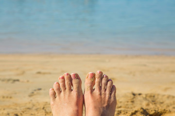 Women's feet in the sand against beach and sea