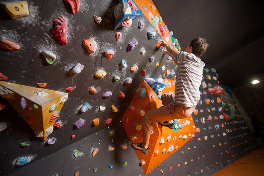 Free climber young man climbing artificial boulder in gym, without special equipment