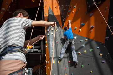 Male with special equipment belaying the climber on rock wall indoors using grigri